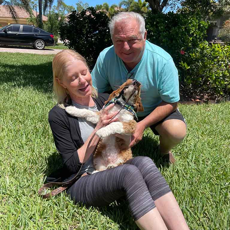 Couple sitting in the grass and holding their dog in their arms